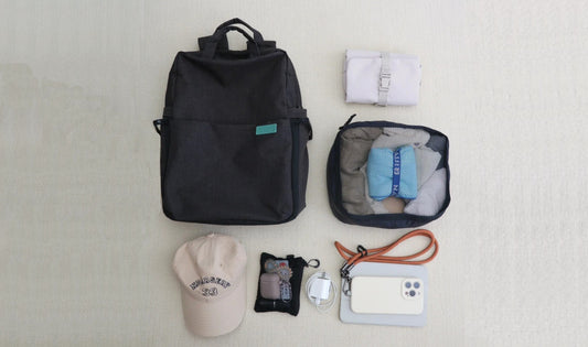 Packed travel essentials in suitcase: legal pad for journaling, pen, books, water bottle, travel pillow, eye mask, and earplugs